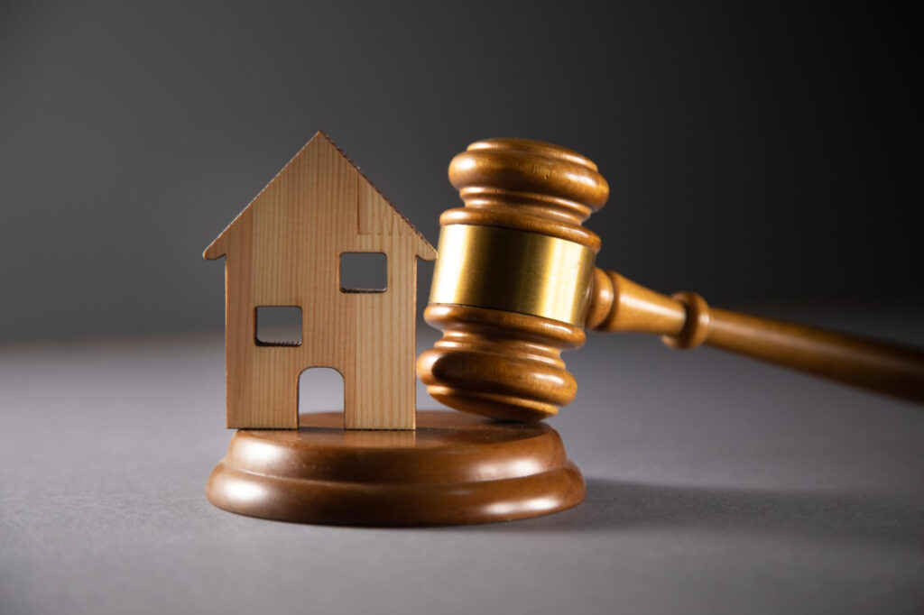 A wooden gavel and a miniature house model on a desk, symbolizing conveyancing and other legal matters related to real estate or property law.