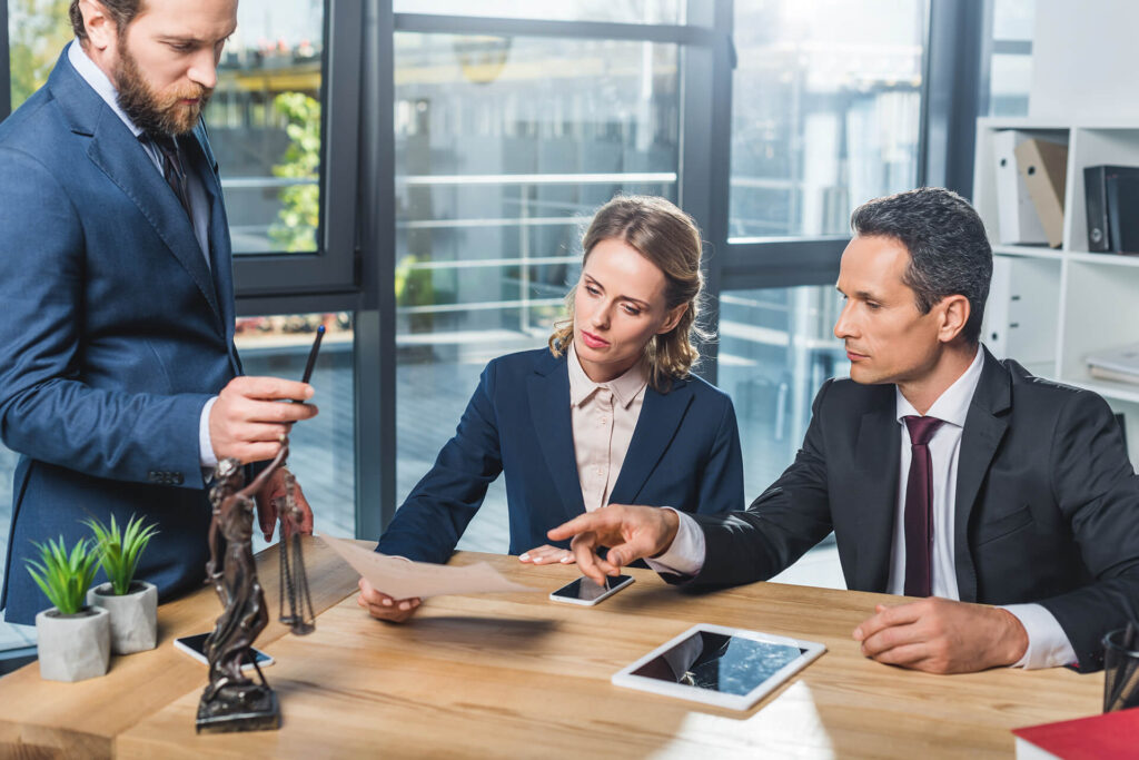 Three business_law professionals discussing over a table in a modern office setting